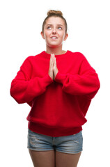 Sticker - Young blonde woman wearing bun and red sweater begging and praying with hands together with hope expression on face very emotional and worried. Asking for forgiveness. Religion concept.