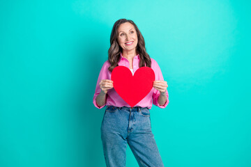 Poster - Photo of adorable lovely woman wear pink shirt holding big red heart looking empty space isolated blue color background