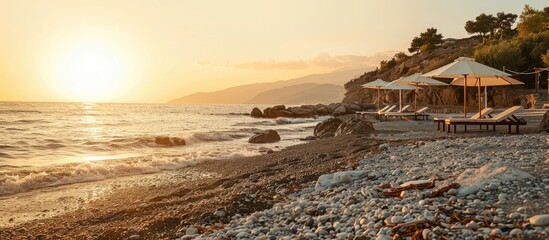 Poster - A rocky shore with pebbled beach at sunset, featuring white umbrellas and sun loungers, offers a tranquil setting with copy space image.