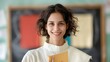 © DARIKA - Indian teacher in a classroom smiling warmly while holding a textbook in front of a colorful chalkboard representing education and passion for teaching Portrait, Realistic Photo, High resolution,