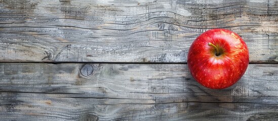 Poster - A vibrant red apple resting on a rustic brown frame atop a gray wooden surface in a top-down view with copy space image included.