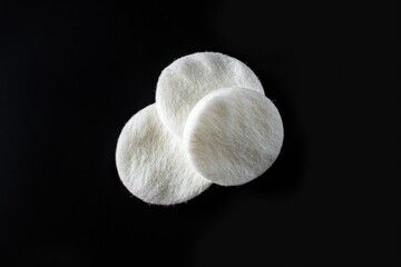Poster - Close-up view of three white wool pads lying on a black surface, suitable for various photography and design uses