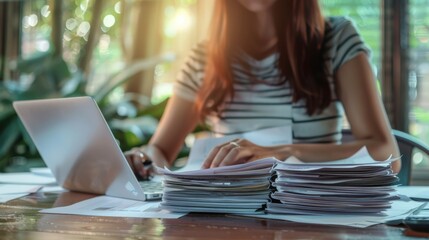 Poster - Close-up of professional woman analyzing tax documents on laptop with sunlight in background. Tax day and financial analysis concept.