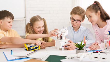 Aufkleber - A group of children, including two girls and two boys, are working on a robotics project in a classroom setting, smiling and appear to be enjoying themselves as they learn and build together.