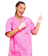 Wall Mural - Young hispanic woman wearing doctor uniform and stethoscope smiling and looking at the camera pointing with two hands and fingers to the side.