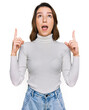 © Krakenimages.com - Young caucasian girl wearing casual clothes amazed and surprised looking up and pointing with fingers and raised arms.