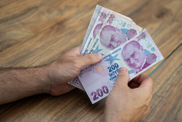 Poster - Male company accountant holds Turkish lira banknotes counting money after currency exchange service with favorable rate sitting at wooden desk in bank office