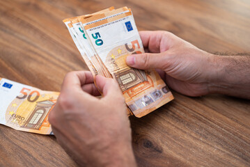 Poster - Male company accountant holds euro bills in hands preparing necessary quantity of money for paying monthly salary to seasonal workers sitting at workplace in office