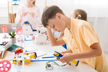 Poster - A young boy is focused on assembling a robot during a robotics class. He is sitting at a table with other students, all working on their own projects.