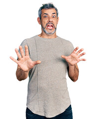 Wall Mural - Middle age hispanic with grey hair wearing casual grey t shirt afraid and terrified with fear expression stop gesture with hands, shouting in shock. panic concept.