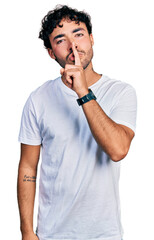 Wall Mural - Hispanic young man with beard wearing casual white t shirt asking to be quiet with finger on lips. silence and secret concept.