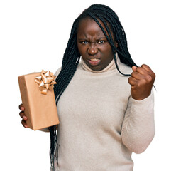 Poster - Young black woman with braids holding gift annoyed and frustrated shouting with anger, yelling crazy with anger and hand raised