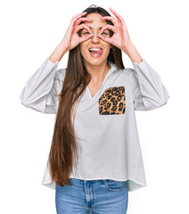 Wall Mural - Young hispanic girl wearing casual clothes doing ok gesture like binoculars sticking tongue out, eyes looking through fingers. crazy expression.