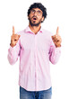 © Krakenimages.com - Handsome young man with curly hair and bear wearing business clothes amazed and surprised looking up and pointing with fingers and raised arms.