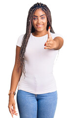 Sticker - Young african american woman with braids wearing casual clothes smiling friendly offering handshake as greeting and welcoming. successful business.