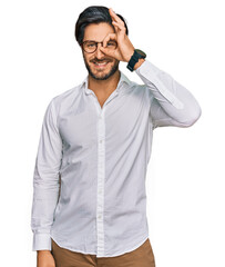 Wall Mural - Young hispanic man wearing business shirt and glasses doing ok gesture with hand smiling, eye looking through fingers with happy face.