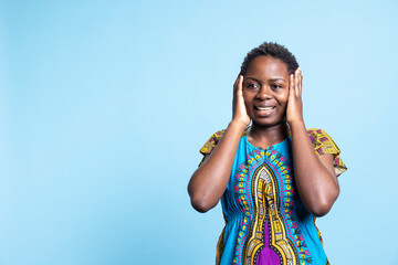 Cheerful woman in fantastic ethnic costume is amazed and overjoyed by something in the studio. After seeing a certain thing, african American girl seems accomplished, excited and impressed.