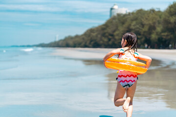 Wall Mural - Happy children kid enjoy and fun outdoor lifestyle travel ocean on summer beach holiday vacation. Portrait of Little cute child girl  with swim ring playing sea water at tropical island in sunny day.