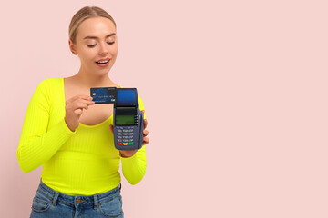 Poster - Pretty young woman with credit card and payment terminal on pink background