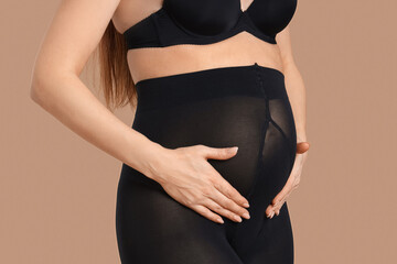 Sticker - Young pregnant woman in black tights on beige background