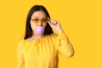 Poster - Beautiful young Asian woman with chewing gum on yellow background