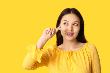 Poster - Beautiful young Asian woman with chewing gum on yellow background