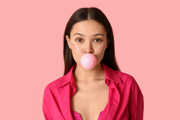 Poster - Beautiful young Asian woman with chewing gum on pink background