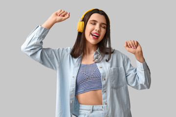 Wall Mural - Happy young woman in modern headphones on grey background