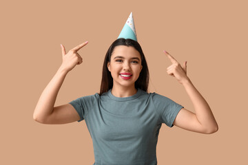 Sticker - Beautiful young woman pointing at party hat on brown background