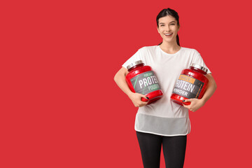 Poster - Happy young woman with bottles of protein powder on red background