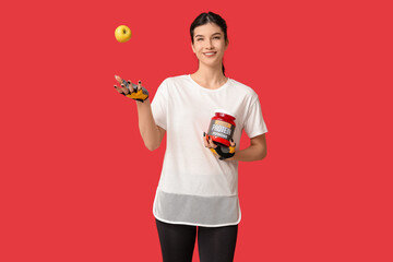 Canvas Print - Beautiful sporty woman with apple and bottle of protein powder on red background