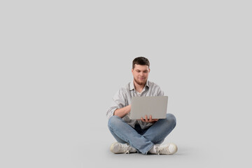 Wall Mural - Young bearded man using laptop on light background