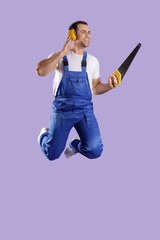 Wall Mural - Young male builder with saw jumping on lilac background