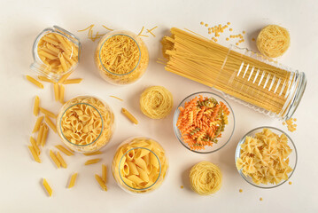 Canvas Print - Composition with different uncooked pasta in glass bowls on light background