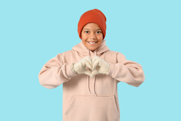 Wall Mural - Cute little happy African-American boy in winter clothes showing heart gesture on blue background