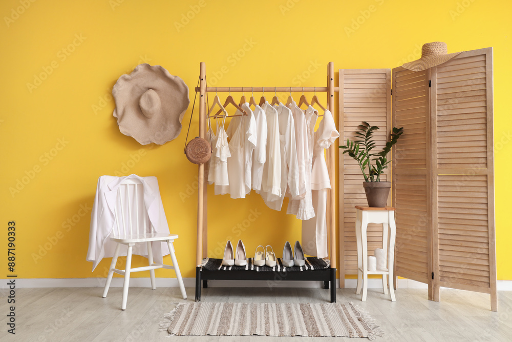 Rack with white clothes near yellow wall in room