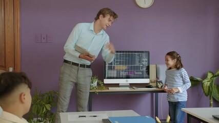Medium long shot of young male Caucasian teacher asking schoolgirl about coding screen at group class