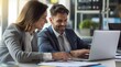© yj - Two business people, a man and a woman, working together using a laptop computer while sitting at a desk in an office. The business concept photo for tech and copy space.