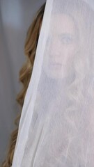 Wall Mural - Vertical slow motion video of woman covered with white mesh fabric. A woman hides her face behind a veil cloth. Female beauty concept.