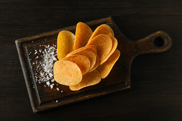 Wall Mural - Potato chips on a wooden board with salt on a dark background