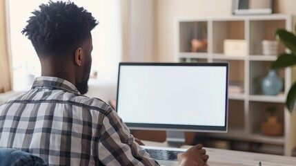 Over shoulder shot of a young man using computer laptop in front of an blank white computer screen in home