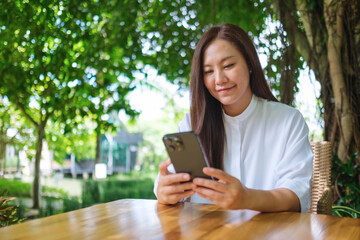 Wall Mural - Portrait image of a young woman holding and using mobile phone in the outdoors