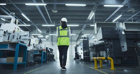 Poster - Female Specialist Walking in a Metal Components Manufacturing Facility. Young Industrial Engineer Wearing a Reflective Safety Vest and a Hard Hat. Follow Footage From the Back