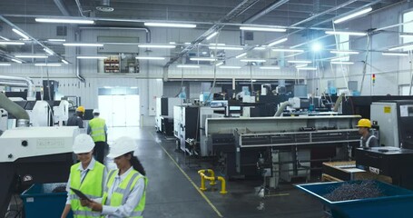 Leinwandbilder - Industrial Manufacturing Facility with Busy Multicultural Workers. Focus on Two Female Employees Having a Conversation and Using a Tablet Computer While They Walk Through the Production Hall