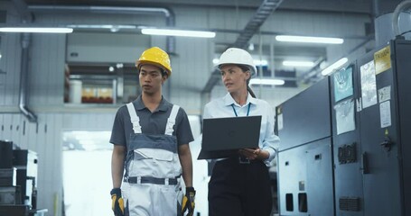 Leinwandbilder - Employees Walking in an Industrial Factory Hall. Caucasian Female Engineer Using a Laptop Computer, Explaining the Work Assignment to a Young Asian Technician. Workers Wearing Hard Hats. Slow Motion