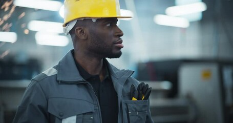 Leinwandbilder - Portrait of an African American Male Engineer in a Yellow Hard Hat and Work Uniform Using a Tablet Computer to Inspect Advanced Machinery in a Modern Factory. Flying Sparks in the Background