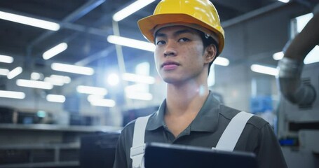 Leinwandbilder - Smart Young Male Engineer in a Yellow Hard Hat Working in a Modern Metal Component Production Factory. Asian Man Looking Around the Facility, Checking Online Data on a Tablet Computer
