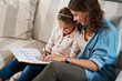 © Chanelle2000/peopleimages.com - Mother, girl and homework on couch for writing, learning and happy with bonding, help and care in family home. Woman, mom and child with education, drawing and pattern for advice with book in Munich