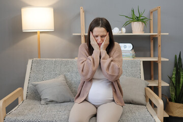 Sad upset pregnant woman wearing casual clothes sitting comfortably on sofa at home expressing negative emotions crying with despair on her face feeling bed