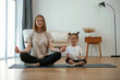 © standret - Calm, in lotus pose. Young woman with little girl are doing yoga at home
